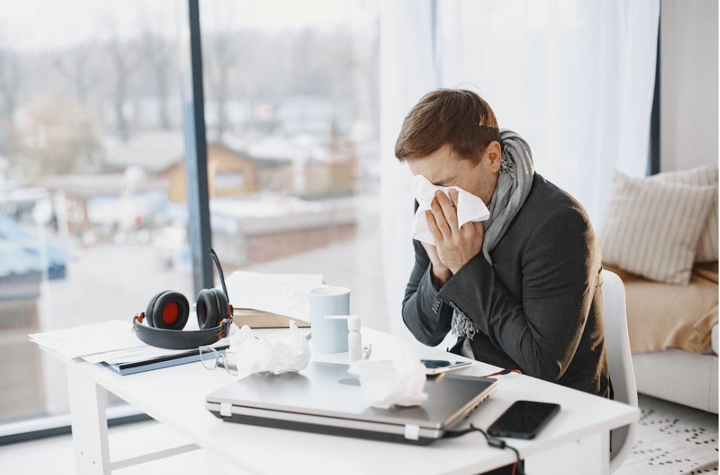 A person blowing their nose and feeling unwell due to the effects of sick building syndrome. 