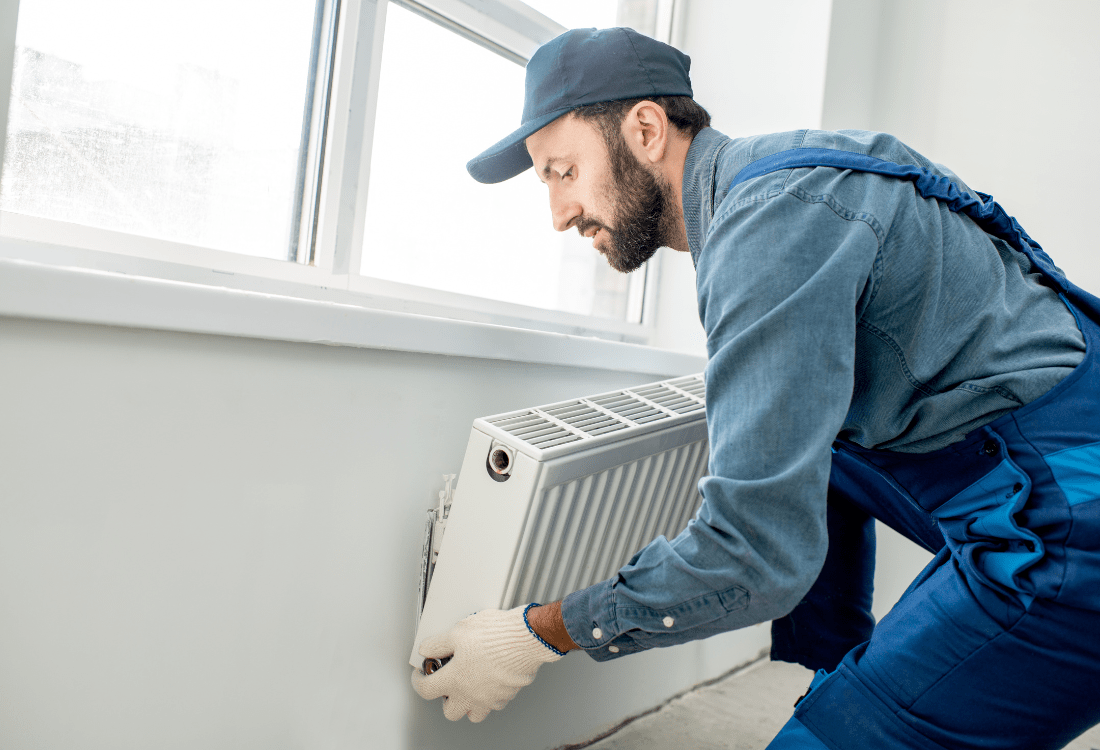 : A skilled workman meticulously mounting a radiator in an office setting, underscoring the importance of professional servicing for optimal heating efficiency and workplace comfort.
